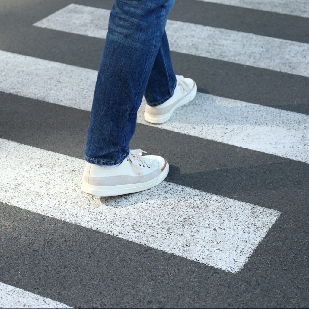 Man in jeans and sneakers walking on crosswalk